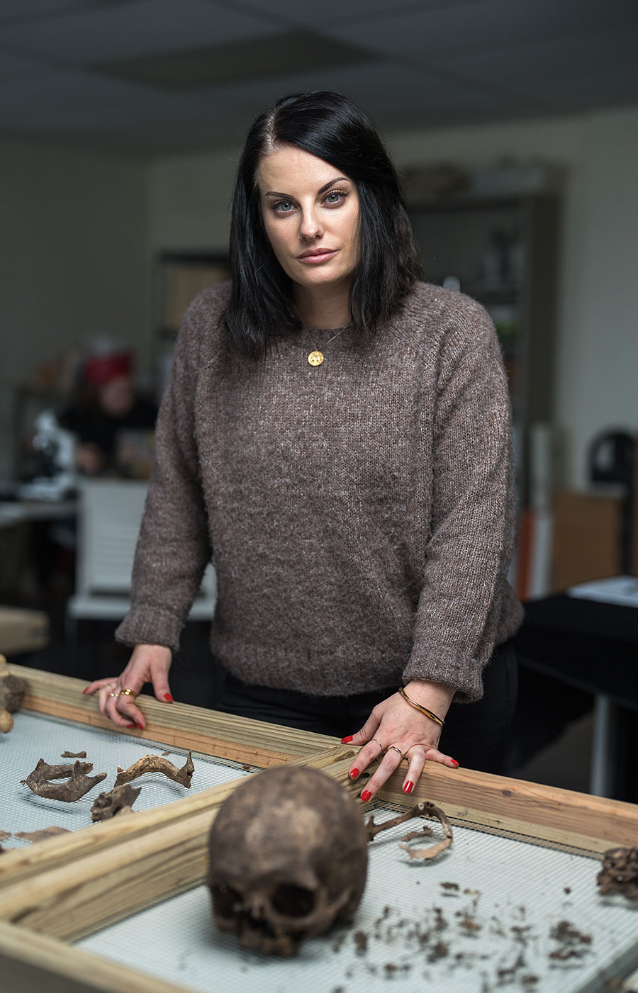 Amy Michael in brown sweater standing behind table with human skull and bone remnants